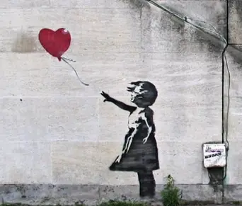 A black stencil of a small girl on a grey concrete wall, reaching out towards a red heart-shaped balloon floating away from her.