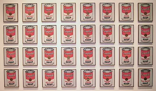 A museum wall hung with 32 small paintings of red and white Campbell's soup cans in four neat rows, each can showing a different flavour.