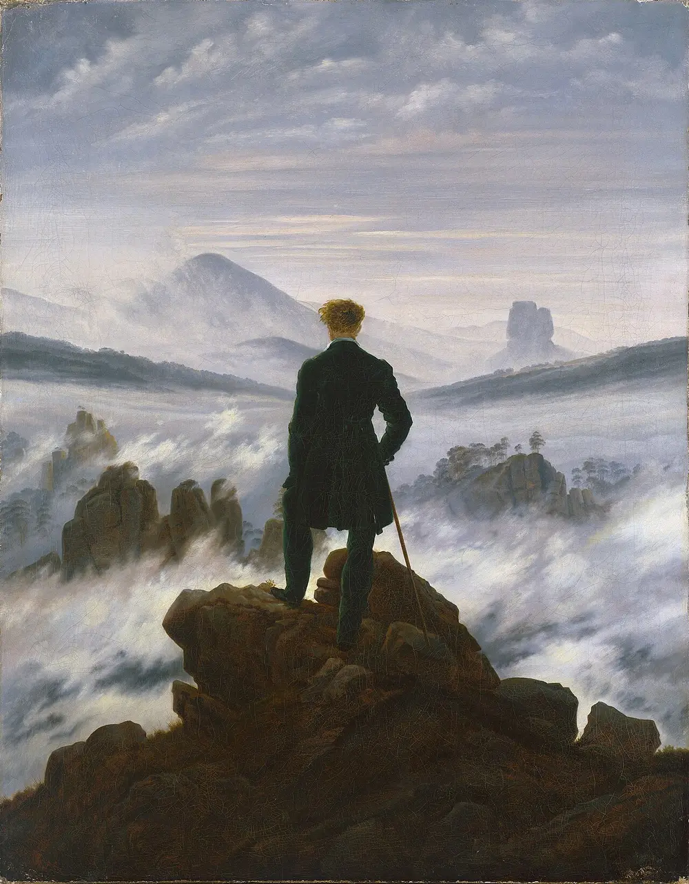 A man in a dark green coat, seen from behind, stands on a rocky peak with a walking stick, looking out over a sea of fog with mountain tops rising through it.