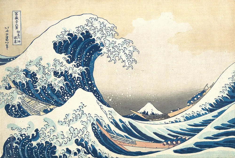 A huge blue wave with claw-like white foam curls over three long boats full of rowers, while small snow-capped Mount Fuji sits low in the distance; Japanese writing is in the top left corner.