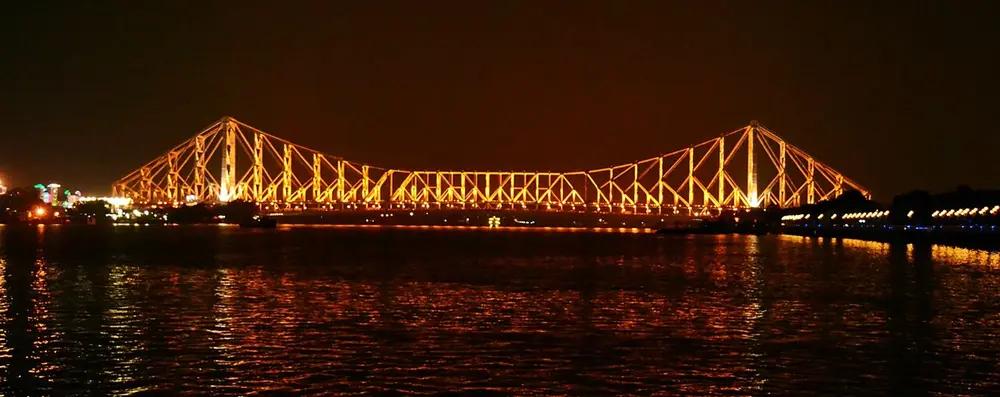 A large steel bridge lit up in gold at night over a dark river.