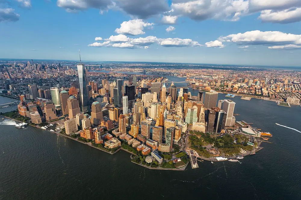 An aerial view of the skyscrapers of Lower Manhattan on the tip of an island, surrounded by water.