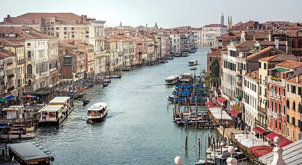 A wide canal lined with old palaces, with boats and gondolas moored along the edges.