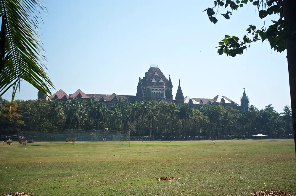 The long Gothic building of the Bombay High Court, with a tall central tower and pointed turrets, seen across the wide green lawn of the Oval Maidan.