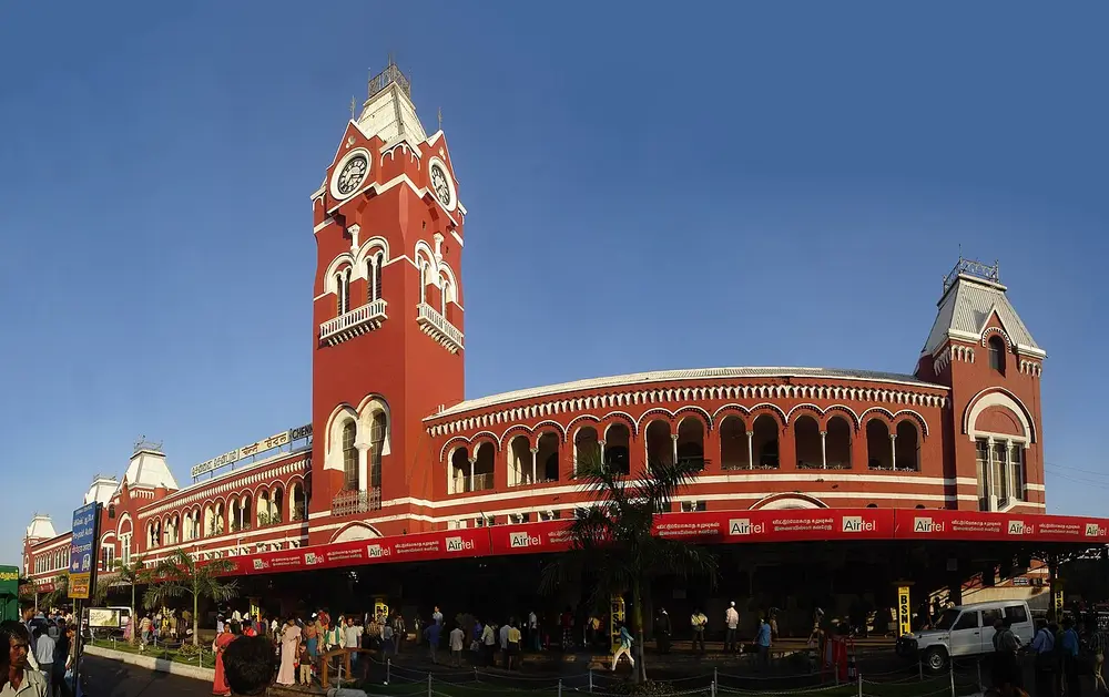 Chennai Central station, a long red building with white trim, a row of round arches and a tall red clock tower with a pointed roof at one end.