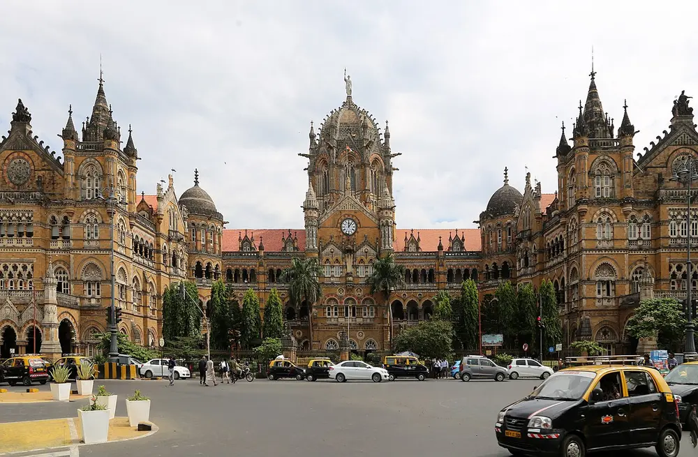 The Chhatrapati Shivaji Maharaj Terminus, a huge stone railway station with a large central dome, pointed arches, turrets and spires, with yellow-and-black taxis in front.