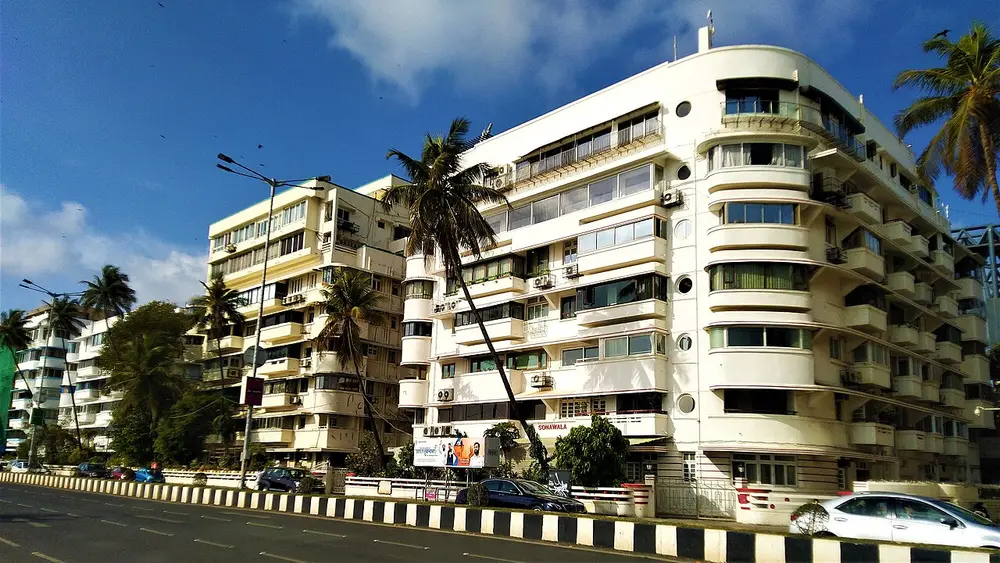 Cream-coloured Art Deco apartment blocks with curved balconies and rounded corners along Marine Drive, with palm trees and the road in front.