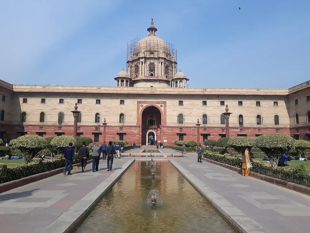 North Block, a long red and cream sandstone building with a domed central tower, seen down a long pool and fountain lined with hedges.