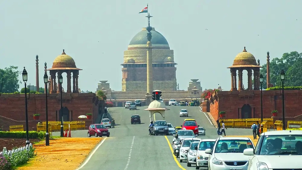 Looking up the avenue to Rashtrapati Bhavan, whose large copper-green dome rises behind red sandstone walls and two small domed kiosks, with a tall column in front.