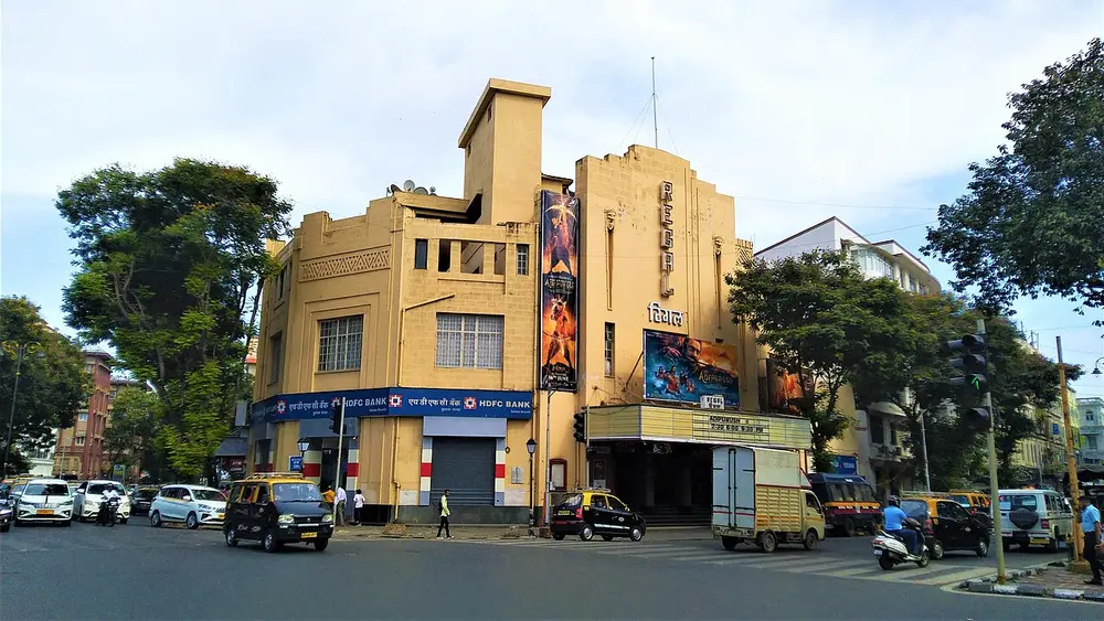 The Regal Cinema at Colaba, a yellow Art Deco building with a tall vertical name sign and stepped blocks, at a street corner with traffic.