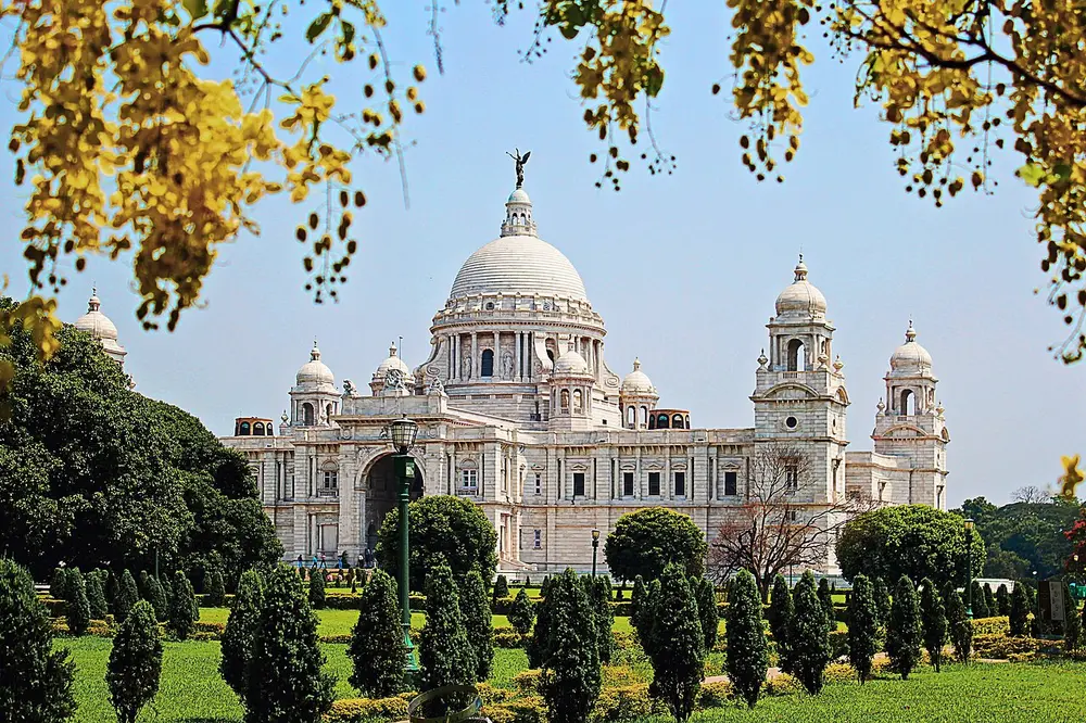 The white marble Victoria Memorial with a large central dome topped by a statue, smaller domed towers at the corners, behind a garden of small clipped trees.