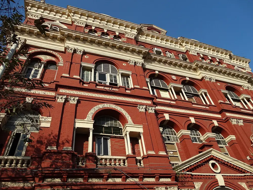 The long red front of the Writers' Building, with rows of tall white-framed windows, white columns and decorated pediments, against a blue sky.