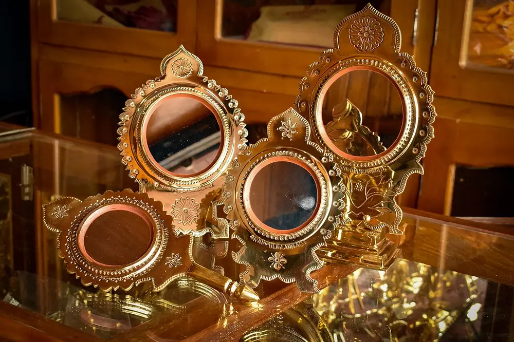 Several round, polished metal mirrors in ornate golden brass frames with leaf-shaped tops, standing on a glass shelf.