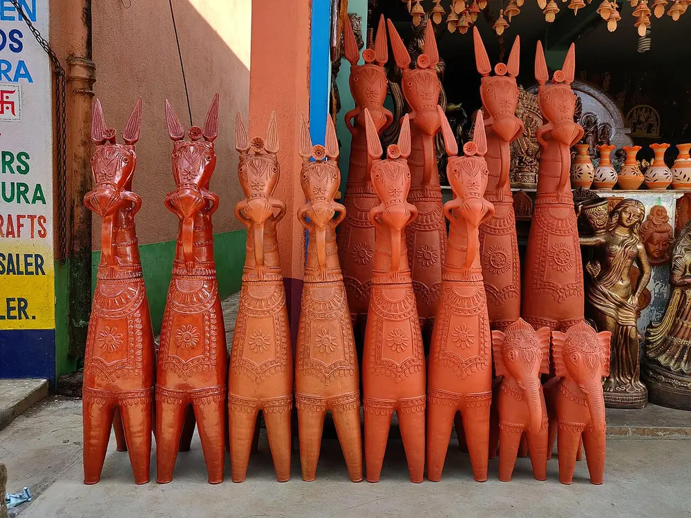 A row of tall, orange-red terracotta horses outside a shop, with long straight necks, upright pointed ears and small stamped patterns.