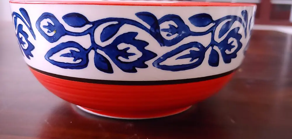 A white bowl painted with dark blue leafy scrolls, with a bright orange-red lower half.