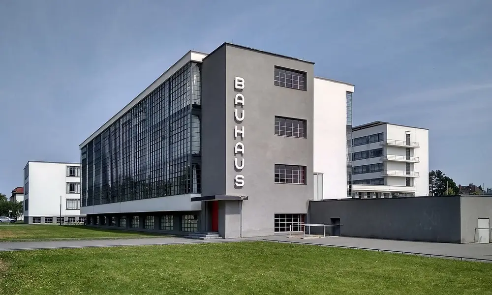 A white and grey modernist building with a tall glass wall on one wing and the word BAUHAUS written down its side in vertical letters.