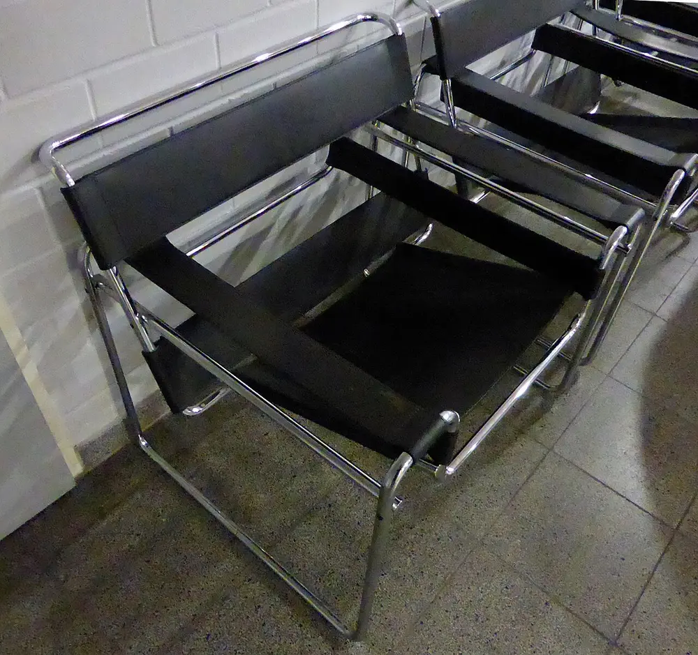 An armchair with a frame of shiny bent steel tube and a seat, back and arms made of tight black leather straps.