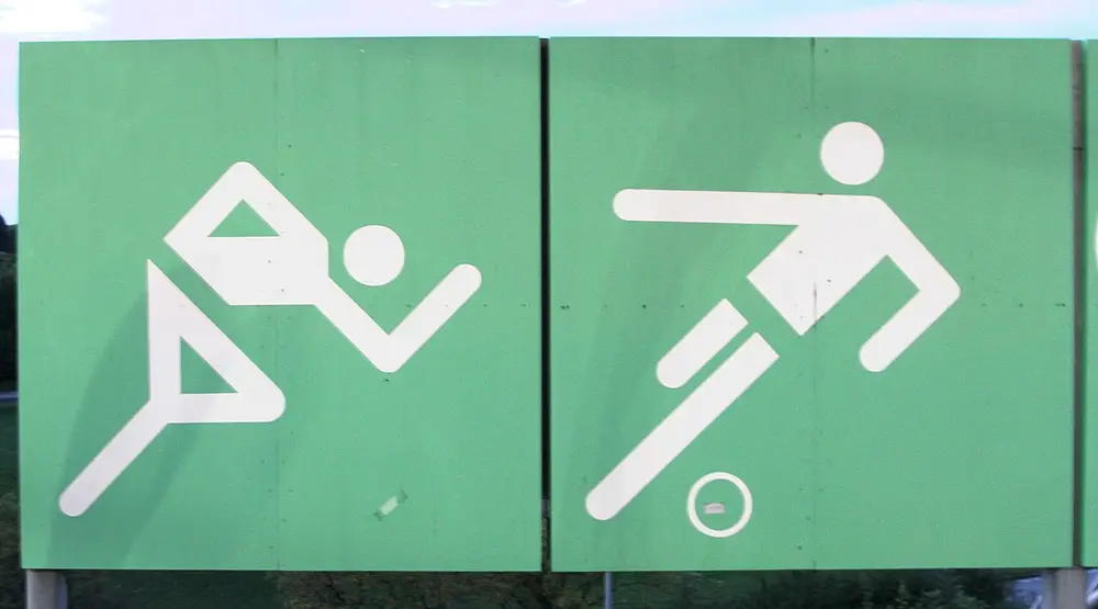 Two large green signs with white stick figures built from straight bars and circles: a runner leaning forward and a footballer kicking a ball.