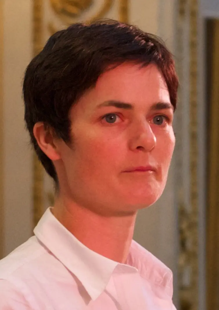 A woman with short dark hair in a white shirt, looking ahead calmly.