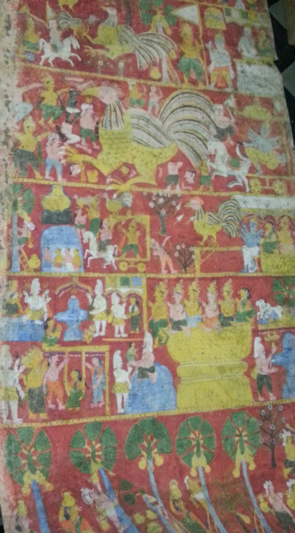 A worn vertical cloth scroll with bands of small figures, animals, birds and buildings on a bright red ground.