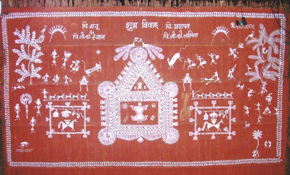 A red-brown mud wall painted in white, with a square shrine at the centre, smaller squares on each side, and rows of tiny stick figures, trees and animals around them.