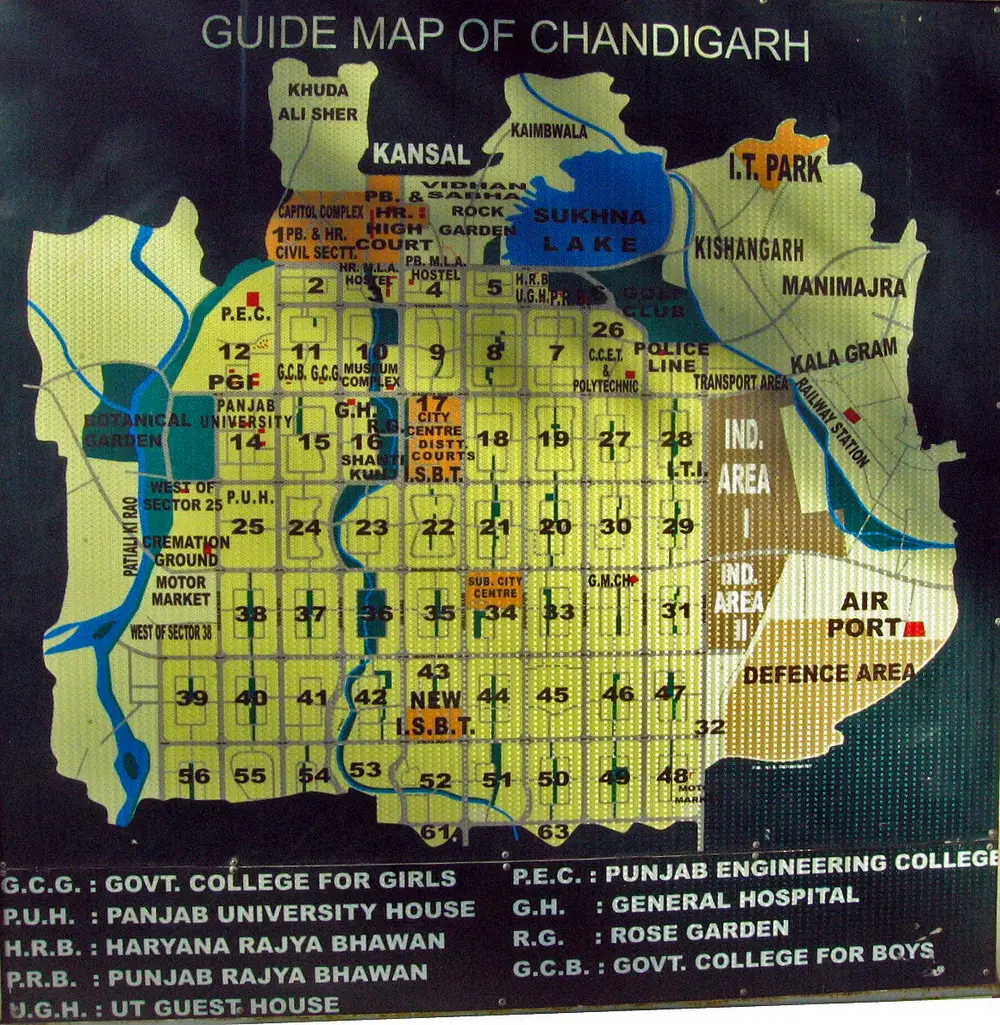 A city guide map of Chandigarh on a board, showing the city as a grid of numbered rectangular sectors, with Sukhna Lake at the top and the airport and industrial area at the edges.