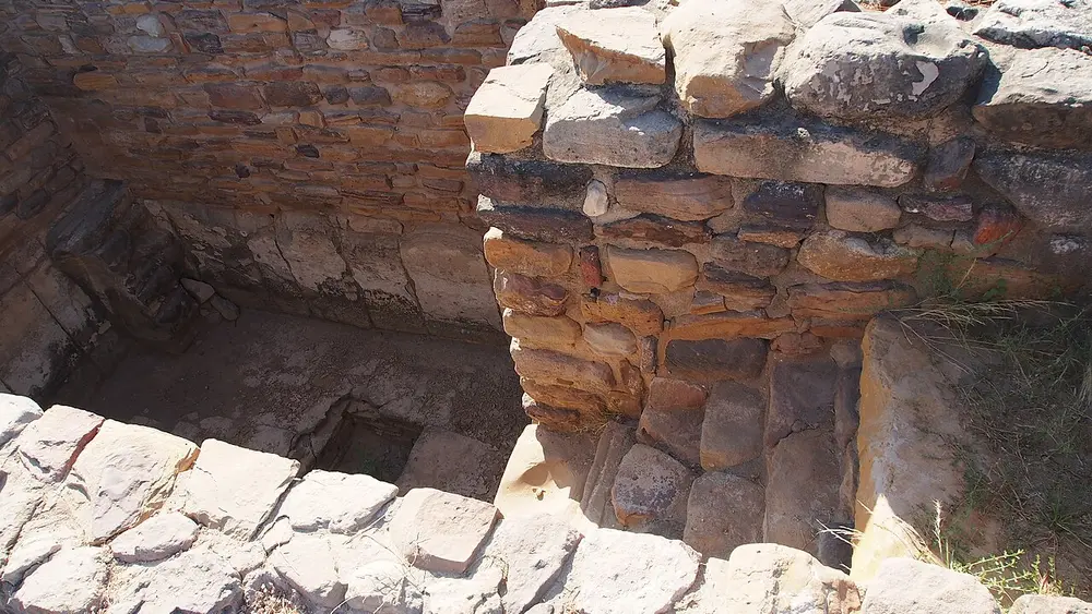 A deep rectangular tank built of rough stone blocks, with stone steps leading down into it, at an ancient ruined site.
