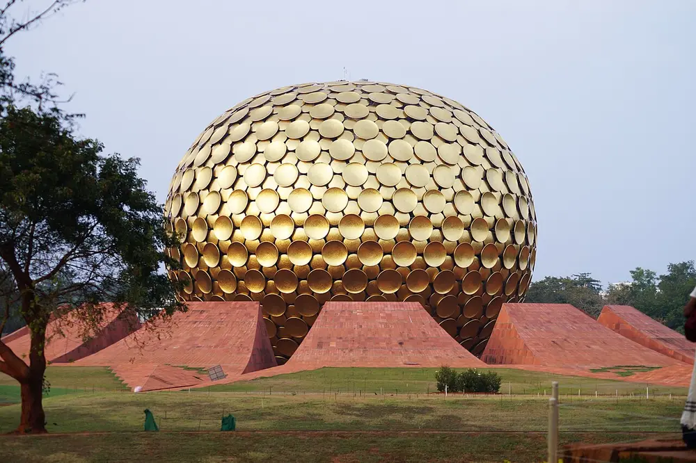 A huge golden globe made of round gold discs, rising out of a ring of curved red earth mounds on a green lawn.