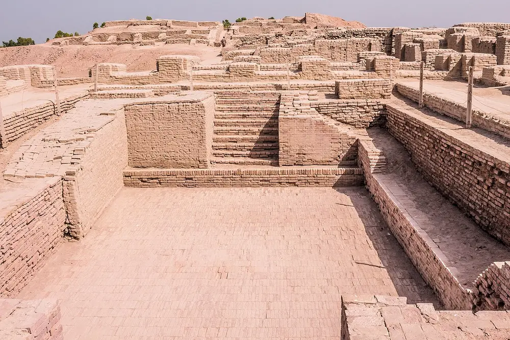 The ruins of a large rectangular brick tank with steps leading down into it at one end, surrounded by low brick walls of rooms.