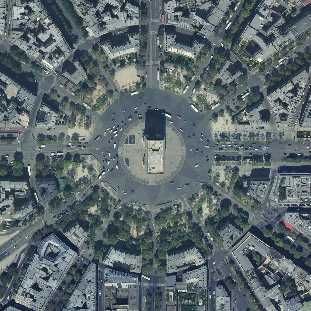 An aerial photo of a huge round junction with a monument in the middle, from which twelve straight avenues spread out like the points of a star between blocks of buildings.