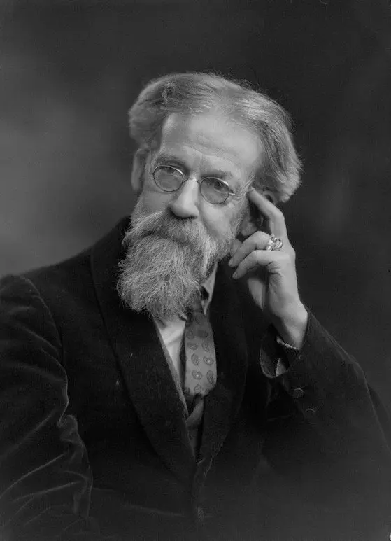 A black and white photo of an old man with a long white beard and glasses, resting his head on his hand.