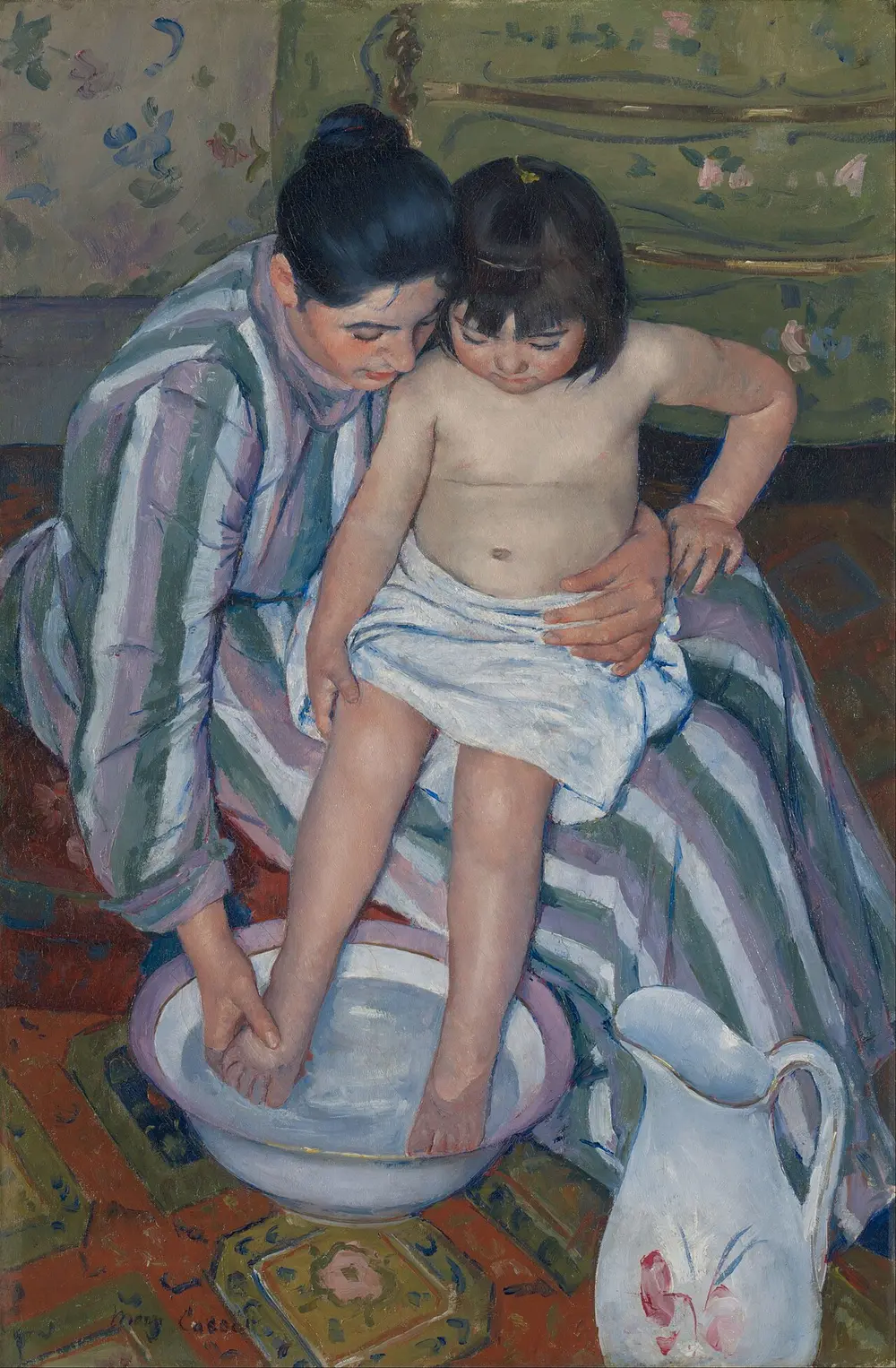Seen from above, a woman in a striped dress holds a small child on her lap and washes the child's feet in a white basin, with a flowered jug on the patterned rug.