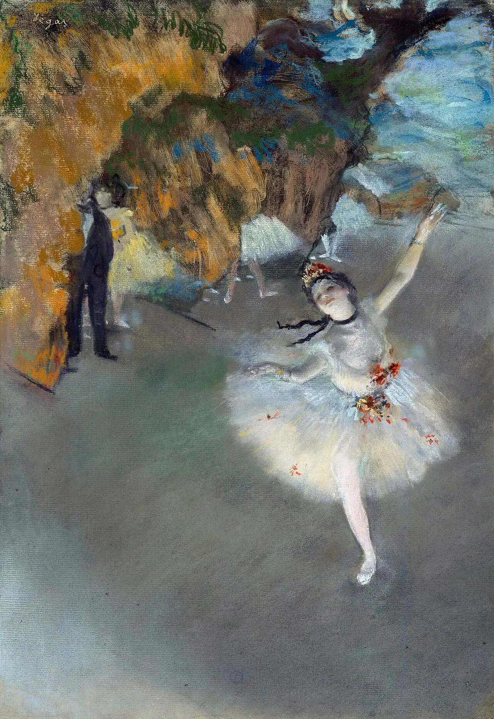 A ballet dancer in a white tutu poses on one leg on a stage, seen from above, while other dancers and a man in a black suit wait behind the painted scenery.