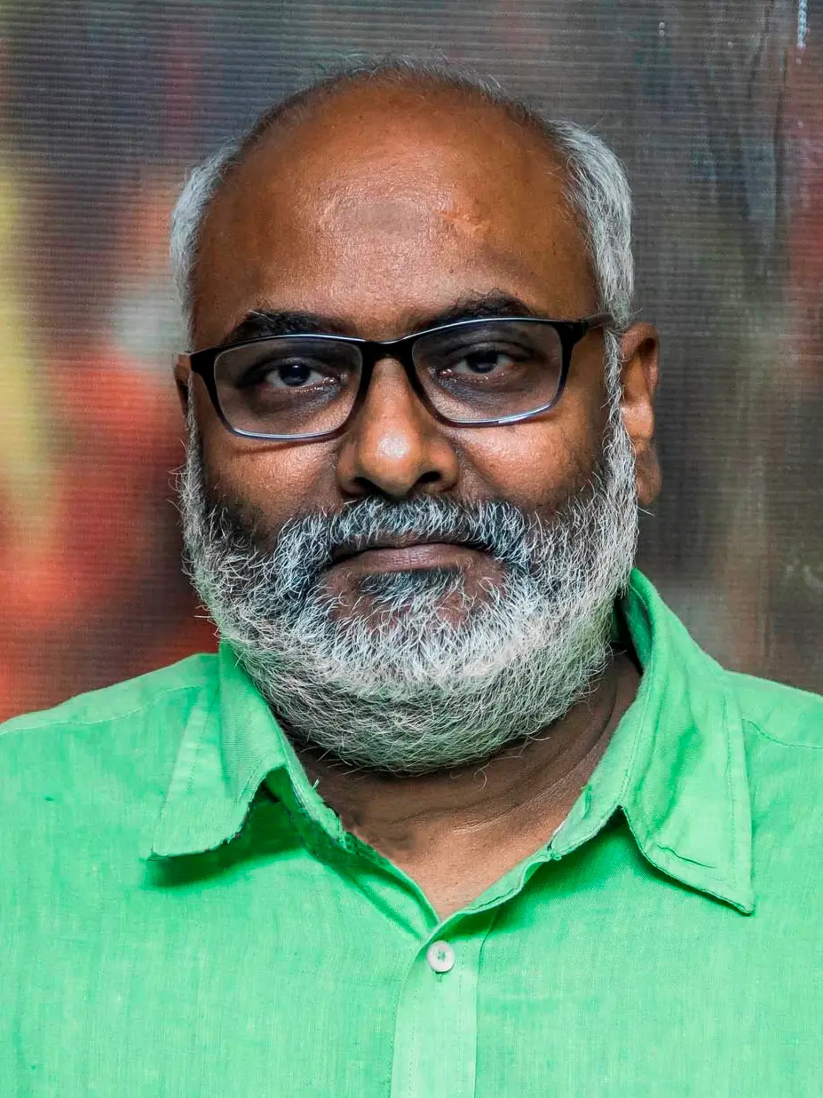 A portrait of the composer M.M. Keeravani with grey hair, a grey beard and glasses, in a green shirt.