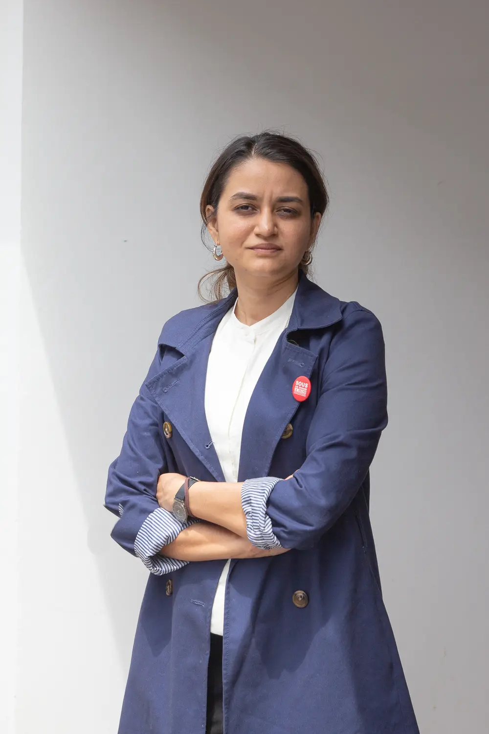 The director Payal Kapadia standing with her arms folded in a navy blue coat over a white top, in front of a plain white wall at Cannes in 2024.