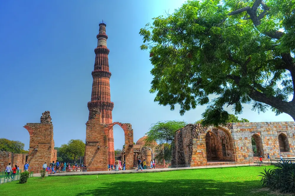 The tall, tapering red sandstone Qutb Minar rising beside ruined arches and walls, seen across a green lawn.