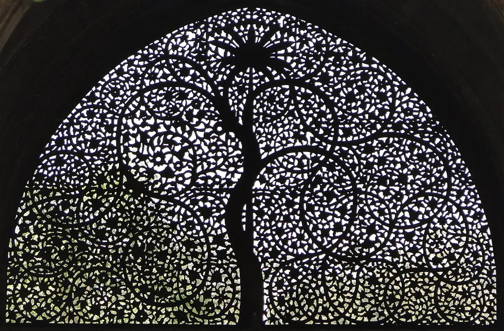A half-round stone window carved into a lacy pattern of a tree with curling branches and leaves, with light shining through the holes.