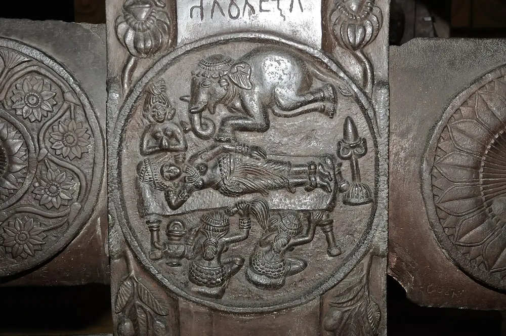 A round stone relief on a railing post showing a woman lying on a bed, a small elephant coming down above her, and seated women at the bottom, with flower medallions on either side.