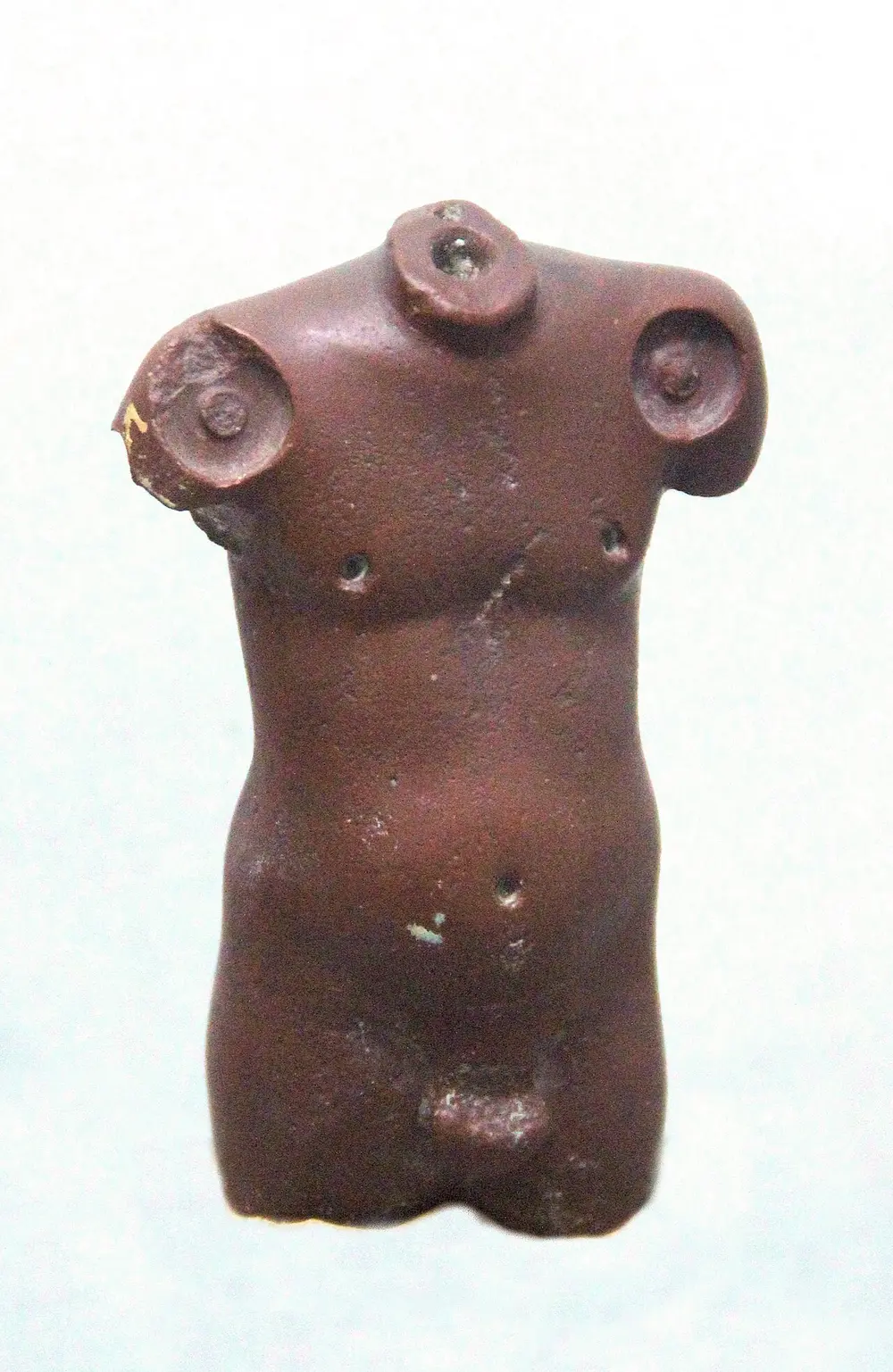 A small headless and armless male torso of polished reddish stone, with round sockets at the neck and shoulders and a slightly rounded belly.