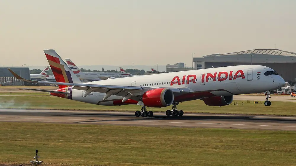 A white Airbus A350 jet with the airline's name in big red letters along its body, red engines and a red, purple and gold tail, speeding along a runway at London Heathrow.