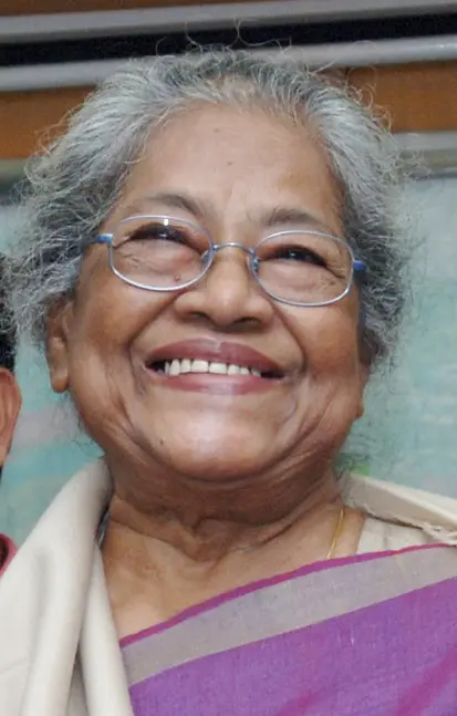 Arpita Singh, an elderly woman with grey hair and glasses, smiling, wearing a cream and purple sari.