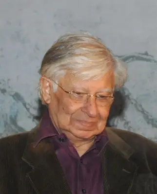 Krishen Khanna, an elderly man with white hair and glasses, wearing a brown jacket.