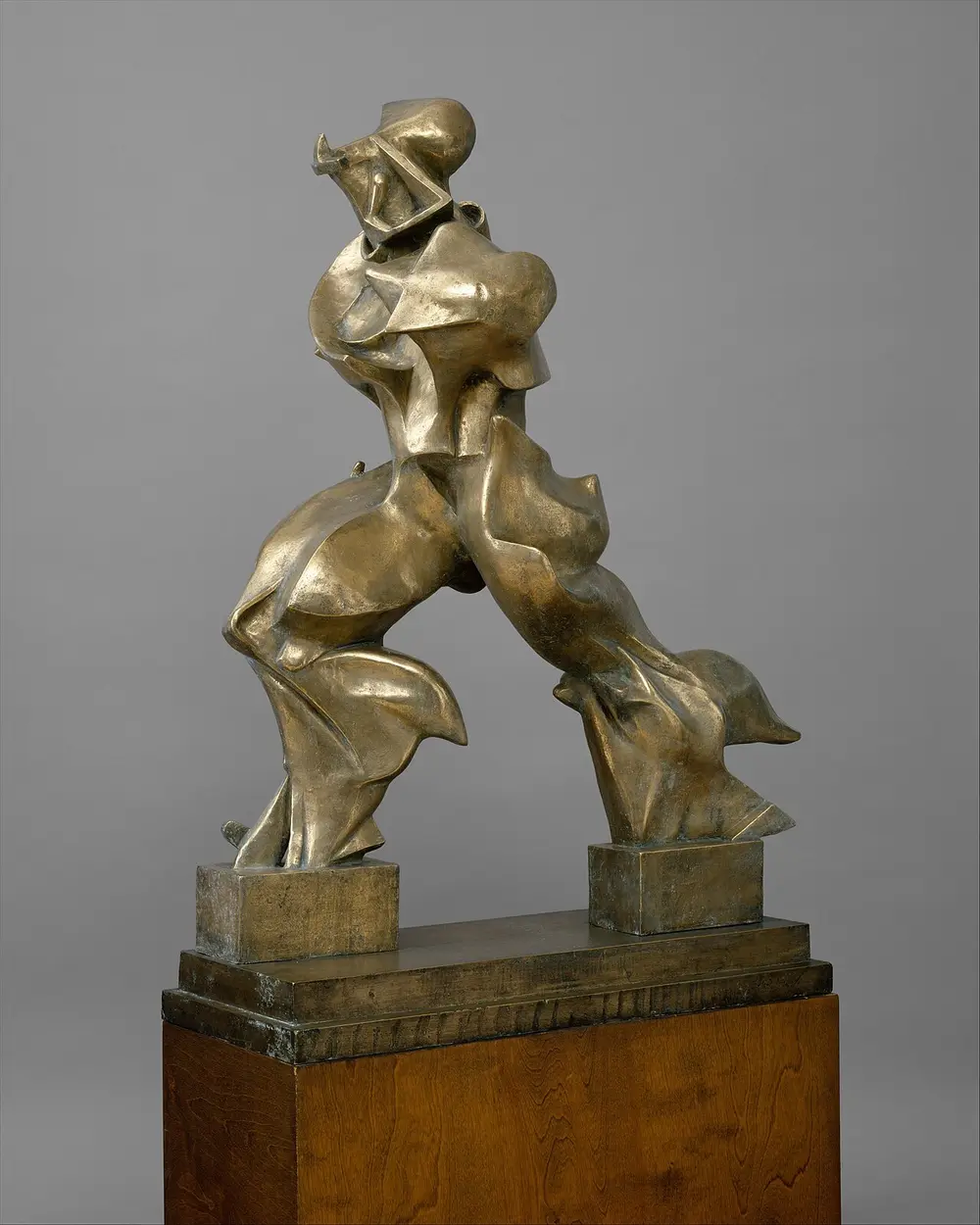 A bronze striding figure with no arms, its legs and body stretched into flame-like, wind-blown shapes, standing on two small blocks.