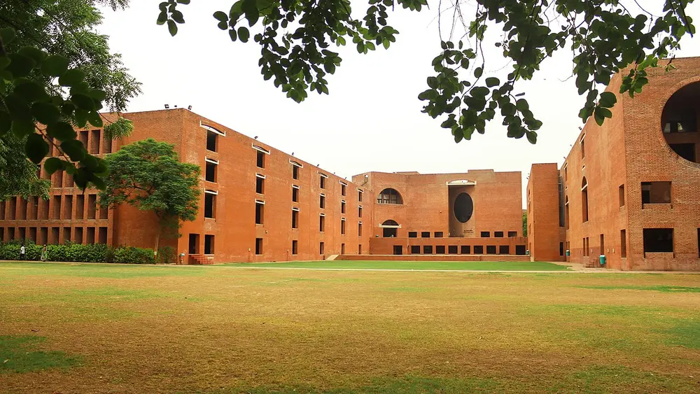 A wide lawn surrounded by tall red-brick buildings with rows of square windows, a large arched opening, a dark circular opening in the far wall and a huge circle cut into the building on the right.