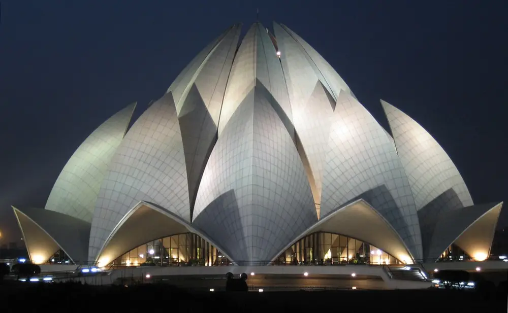 The Lotus Temple lit up at night, a white building made of many large curved marble petals arranged like a half-open lotus flower.
