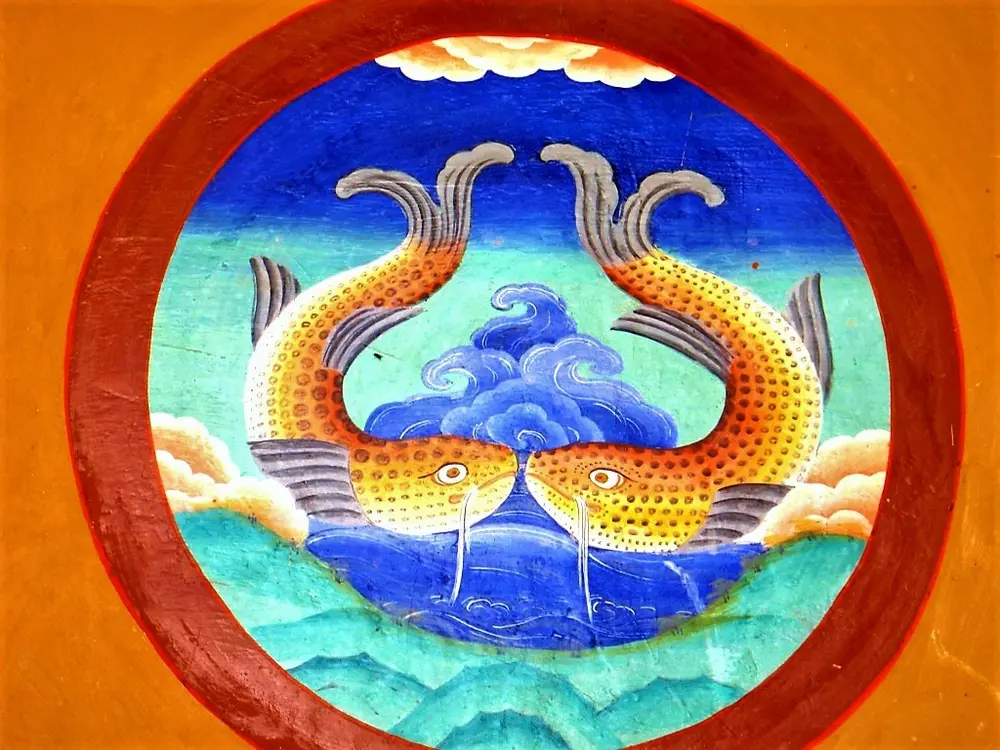 A round wall painting of two orange fish with spotted scales, their tails curling up, facing each other above blue and white waves.