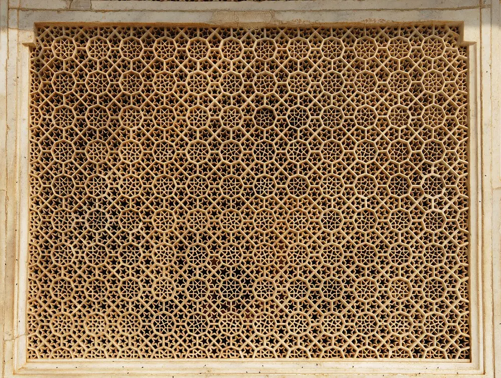 A large white marble window screen cut right through into a dense, even lattice of six-sided and star-shaped holes, set in a plain marble frame.