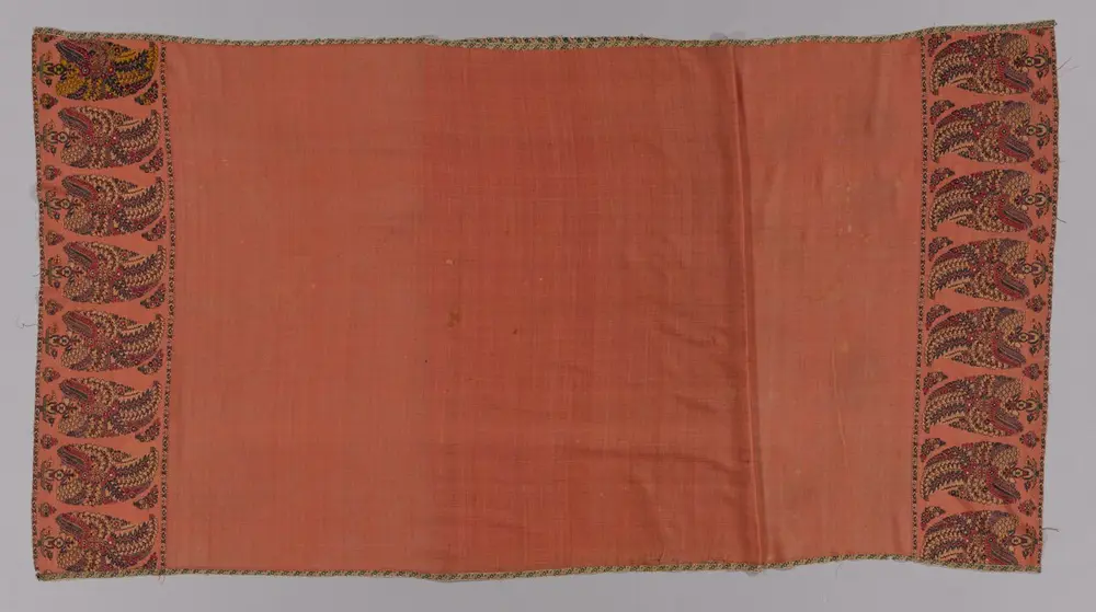 A long apricot-coloured wool shawl with a plain centre. Each end has a deep band of tall, leaning teardrop shapes with curled tips, filled with tiny flowers in red, blue and green.
