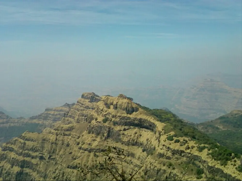 A steep hillside made of horizontal rock layers, like giant steps, fading into haze.