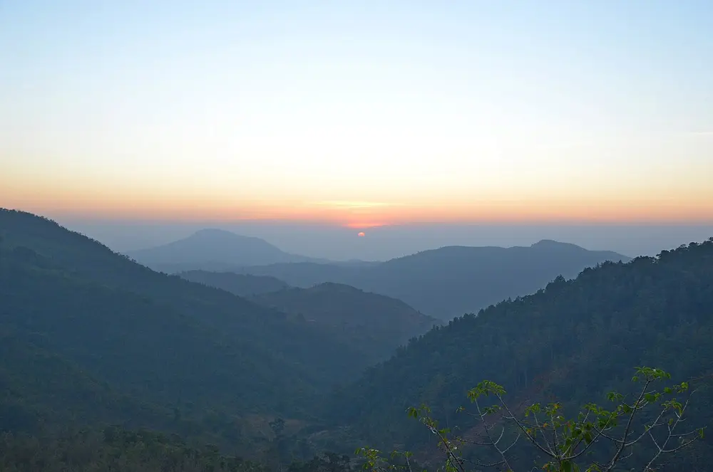 Layers of forested hills fading into haze under an orange sunrise.